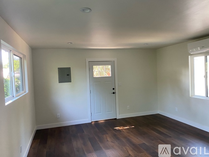 A room with wooden floors and white walls, with a door and a window.