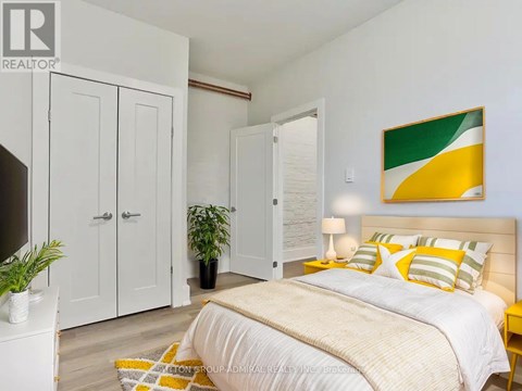 A bedroom with a bed, a lamp, a potted plant, and a painting on the wall.