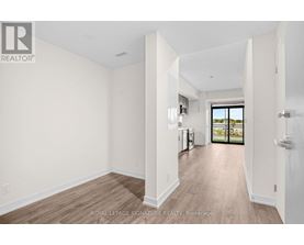 A spacious room with white walls and wooden flooring, leading to a balcony with a view of the outdoors.