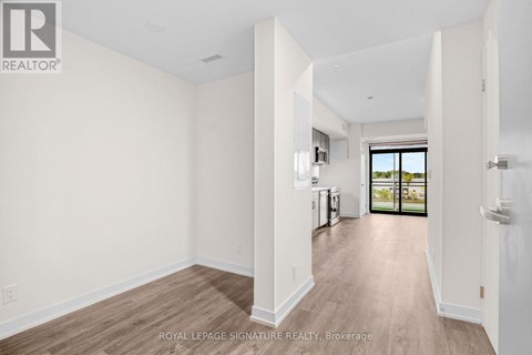 A spacious room with white walls and wooden flooring, leading to a balcony with a view of the outdoors.