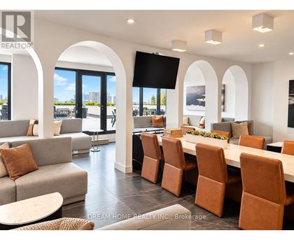 A modern living room with a large couch, a dining table with chairs, and a flat-screen TV mounted on the wall.