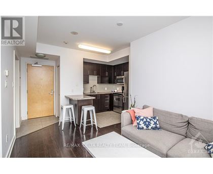A living room with a grey couch and a kitchen area in the background.