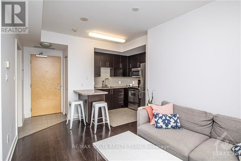 A living room with a grey couch and a kitchen area in the background.