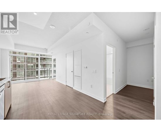 A spacious room with wooden flooring and white walls, with a glass door leading to another room.