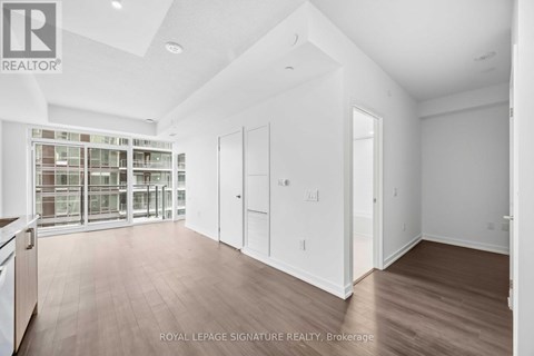 A spacious room with wooden flooring and white walls, with a glass door leading to another room.