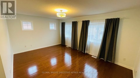 A spacious room with wooden floors and a large window with curtains.