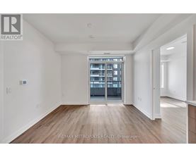 A spacious room with wooden flooring and a large window leading to a balcony.