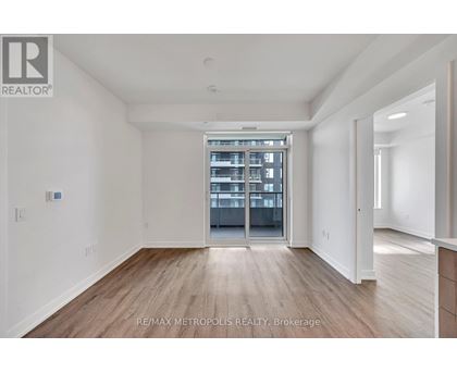 A spacious room with wooden flooring and a large window leading to a balcony.