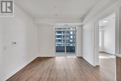 A spacious room with wooden flooring and a large window leading to a balcony.