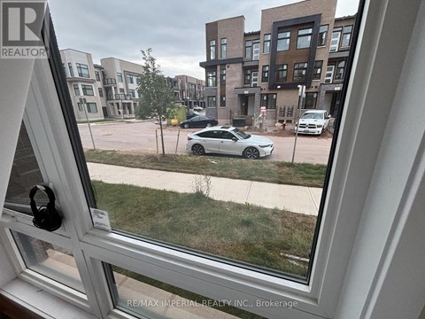 A view from a window looking out at a parking lot with cars and a building in the distance.