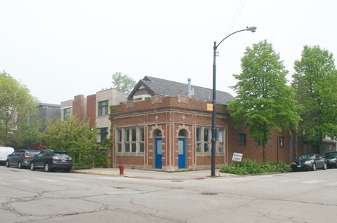 A small brick building with a blue door sits in front of a parking lot.