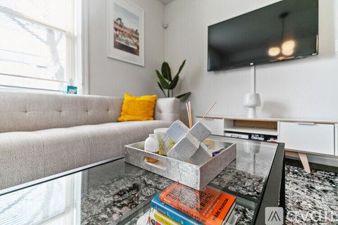 A grey sofa with a yellow pillow sits in a living room with a television and a glass coffee table.