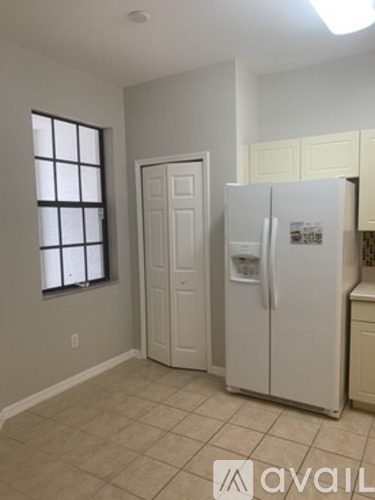 A white refrigerator in a kitchen with beige walls and tile flooring.