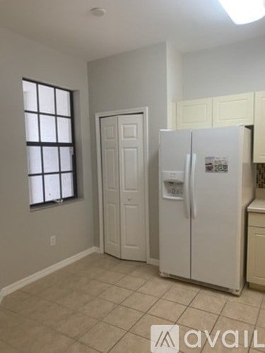A white refrigerator in a kitchen with beige walls and tile flooring.