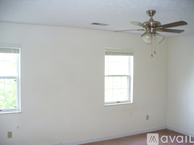 A room with a ceiling fan and two windows.