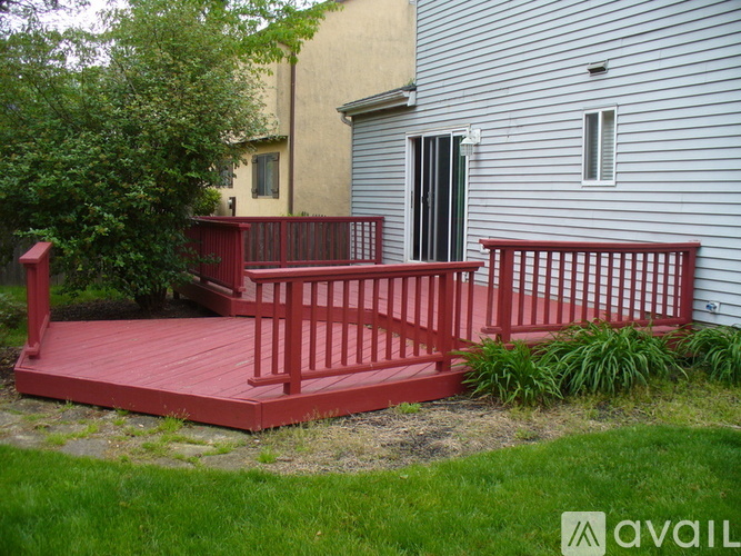 A red deck with a railing and a tree in front of a grey house.