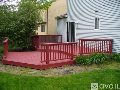 A red deck with a railing and a tree in front of a grey house.