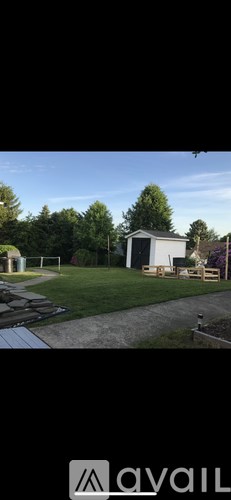 A small white building with a dark roof is surrounded by a grassy area and trees.