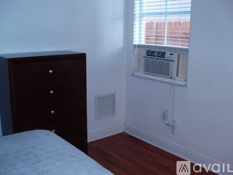 A bedroom with a bed, dresser, and window with air conditioning unit.
