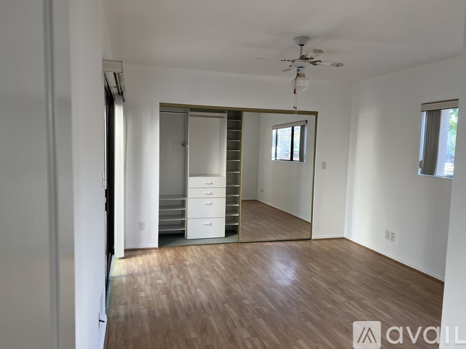 A room with wooden flooring and a white wall with a doorway leading to another room.