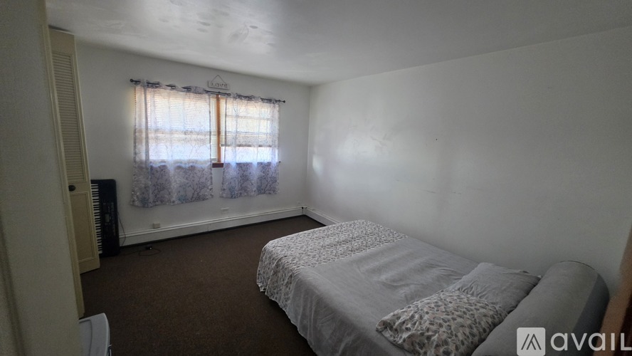 A bedroom with a bed, carpet, and a window with curtains.