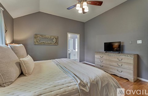 A bedroom with a large bed, a dresser with a television on top, and a ceiling fan.