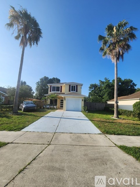 A house with a driveway and two palm trees in front.