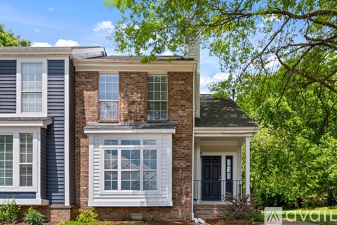 A house with a brick facade and a black door is surrounded by greenery.