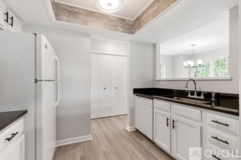 A white refrigerator stands in a kitchen with wooden floors and white walls.