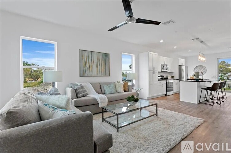 A modern living room with a grey sofa, a glass coffee table, and a ceiling fan.