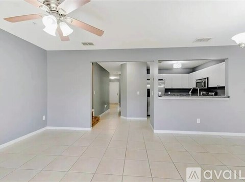 A spacious room with a ceiling fan and a kitchen in the background.