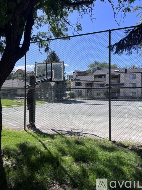 A basketball court surrounded by a fence with trees and apartment buildings in the background.