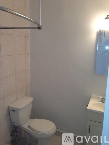 A white toilet in a small bathroom with a white sink and a white cabinet.