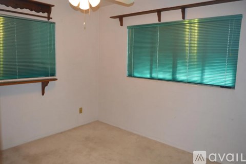 A room with a chandelier and two windows with green blinds.