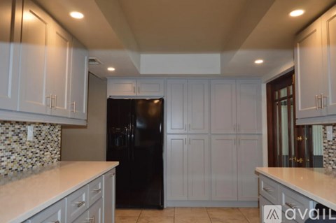 A kitchen with a black refrigerator and white cabinets.
