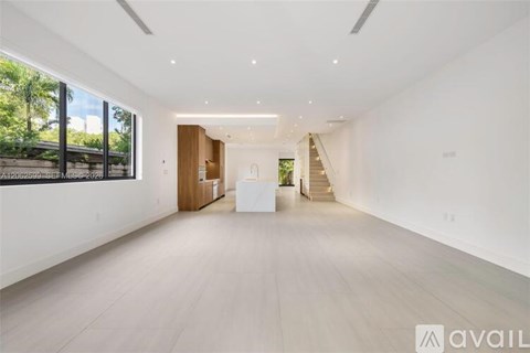 A spacious, well-lit room with wooden floors and a staircase leading to another level.