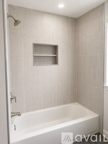 A white bathtub in a bathroom with a shower head and a shelf above it.