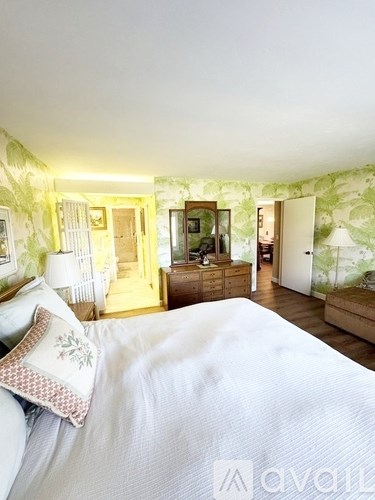 A bedroom with a bed, dresser, and mirror with a green floral wallpaper.