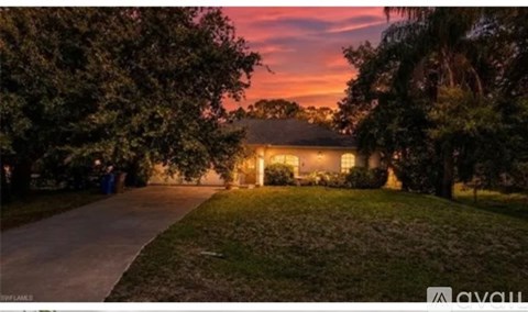 A house is lit up at dusk with trees in the foreground.