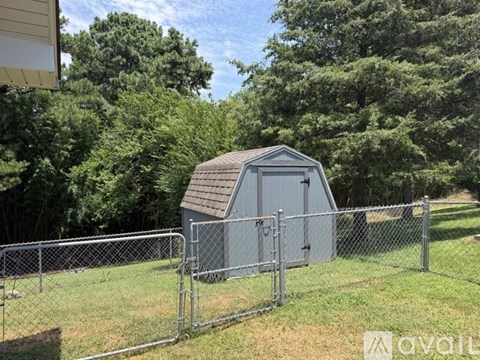 A small grey shed sits behind a chain link fence in a grassy area.