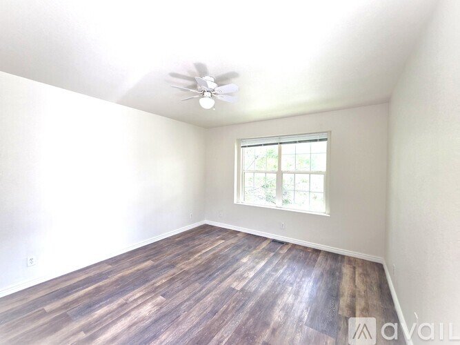 A room with a ceiling fan and a window with a view of trees.