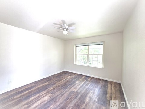 A room with a ceiling fan and a window with a view of trees.