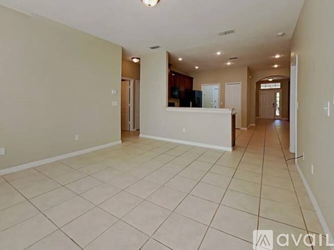 A spacious room with tiled flooring and a kitchen area in the background.