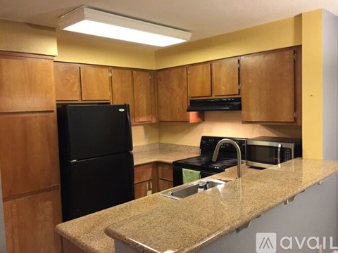 A kitchen with a black refrigerator and wooden cabinets.