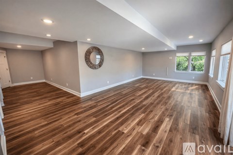 A spacious room with wooden flooring and a round mirror on the wall.