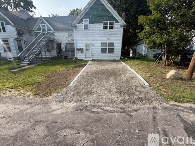 A white house with a green roof and a driveway in front.