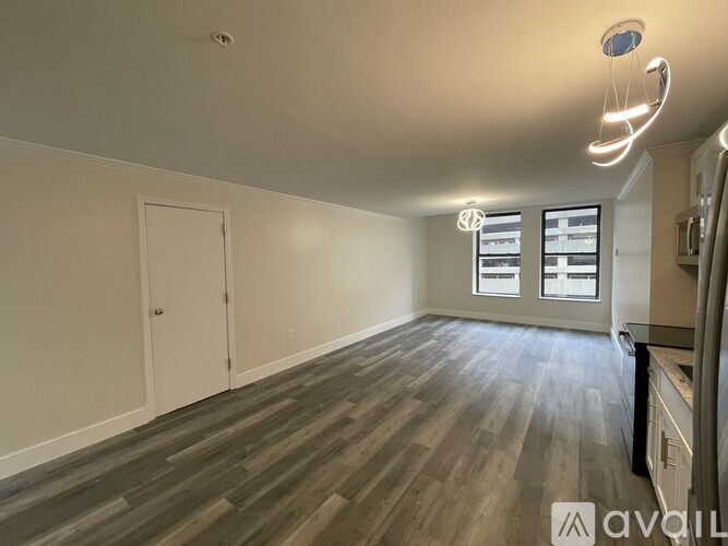 A spacious room with wooden flooring and a window with blinds.
