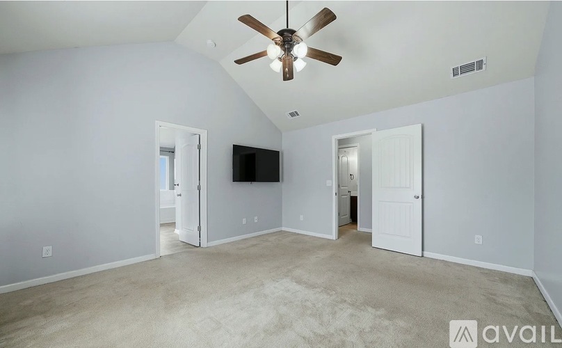 A spacious room with a ceiling fan and a flat-screen TV mounted on the wall.