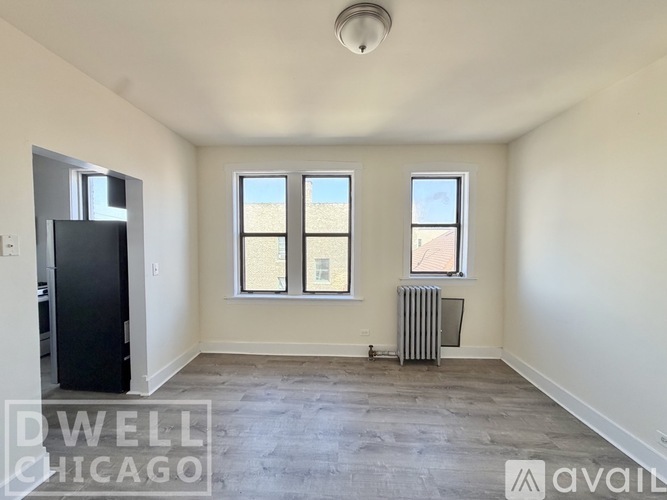 A spacious room with a black refrigerator, two windows, and a radiator.