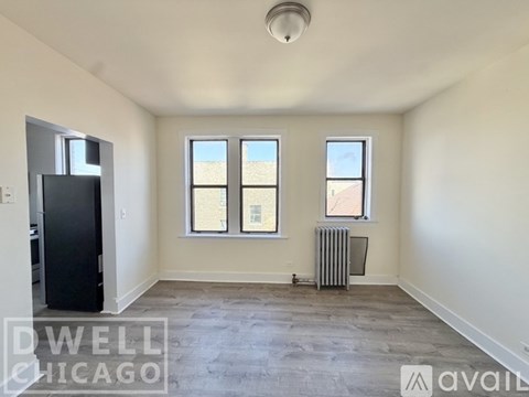 A spacious room with a black refrigerator, two windows, and a radiator.